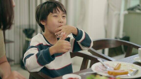 亚洲年轻母亲和她的小男孩花时间在一起吃早餐在家里6岁的小儿子喜欢吃用手指把番茄酱放在碗里玩食物