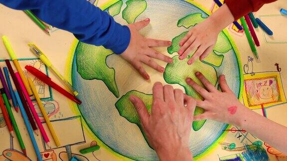 一组孩子和老师的手紧握在他们创作的关于可持续发展的艺术作品上的镜头