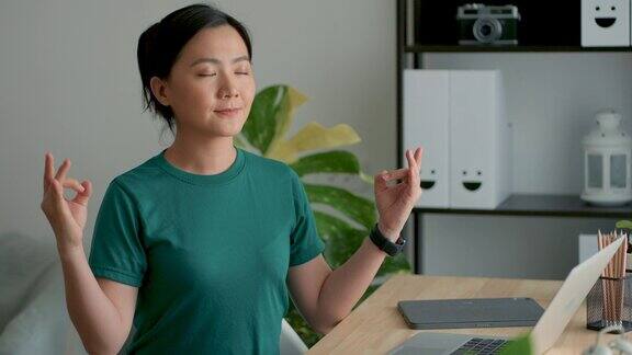 一名亚洲女性坐在家里的办公室里双手做瑜伽姿势深呼吸