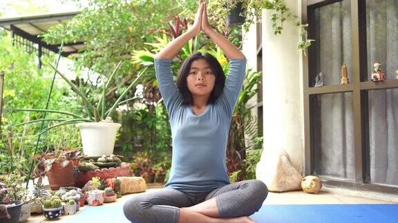 亚洲少女穿着蓝色衬衫在蓝色瑜伽垫上练习合十礼姿势