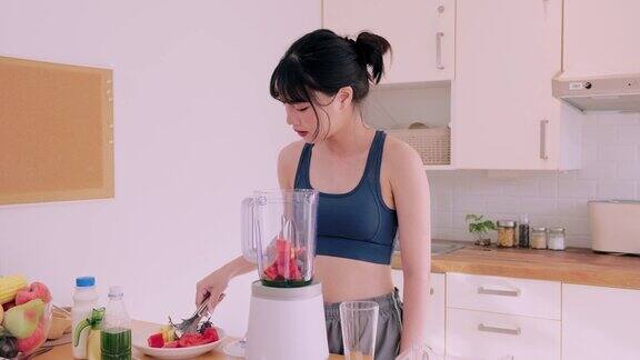 一位穿着运动服的快乐的亚洲妇女将水果和蔬菜混合在一起在她的厨房里品尝着营养丰富的冰沙她崇尚健康快乐的生活方式提倡健康饮食的好处