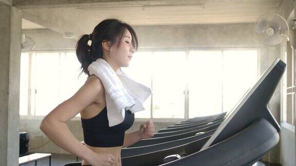 迷人的亚洲女孩在跑步机上跑步在体育馆里慢动作保健运动和运动
