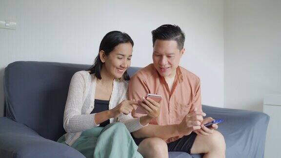 幸福的亚洲夫妇看视频在客厅的智能手机