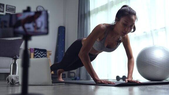 一名亚洲女子在客厅用手机摄像头在线教瑜伽年轻女性穿着运动服在家锻炼观看在线健身教室
