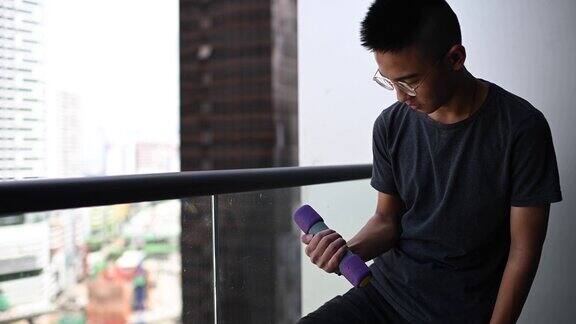 一个亚裔中国少年在阳台上用哑铃锻炼肌肉