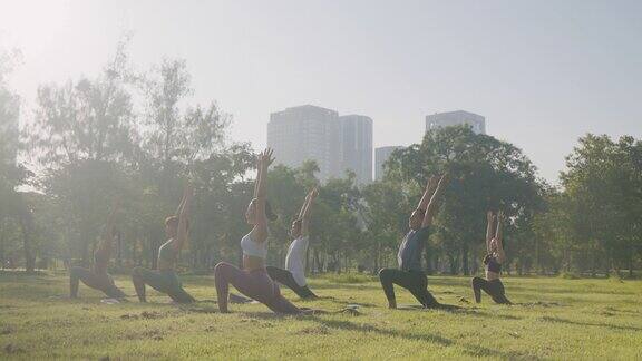 六人组混合年龄的人在城市公园里做瑜伽姿势叫武士姿势以健身、运动、瑜伽和健康的生活方式理念