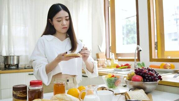 快乐的亚洲妇女在厨房的面包上涂果酱健康的饮食和健康