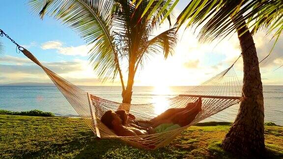 幸福的年轻夫妇放松在热带吊床日落