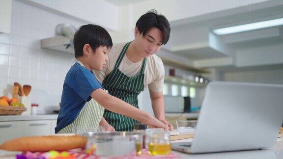 爸爸和可爱的小儿子正在平板电脑上通过社交媒体上的视频一起在厨房做饭和学习烹饪概念和家庭时代