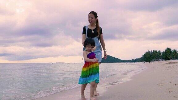 年轻的母亲和女儿手牵着手走在海滩上