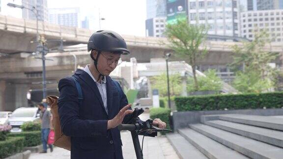 亚洲男子用手机到达目的地在大城市里骑电动车