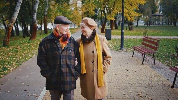 幸福的退休夫妇穿着温暖优雅的外套在河边的城市公园里浪漫地散步谈笑风生