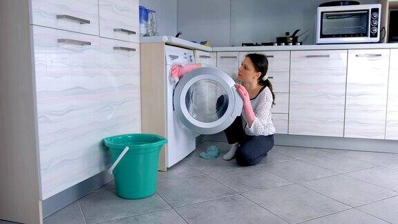 戴着粉红色橡胶手套的妇女坐在地板上用布洗洗衣机