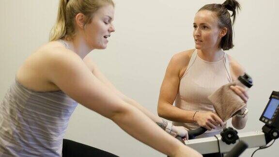在私人教练的指导下一名女子在健身室的固定自行车上锻炼