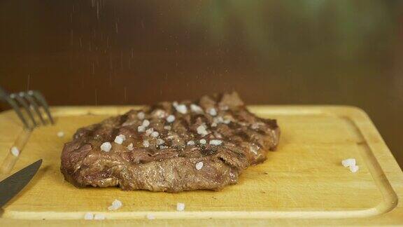 手盐牛排盐慢慢地落在肉上肉放在一块木板上