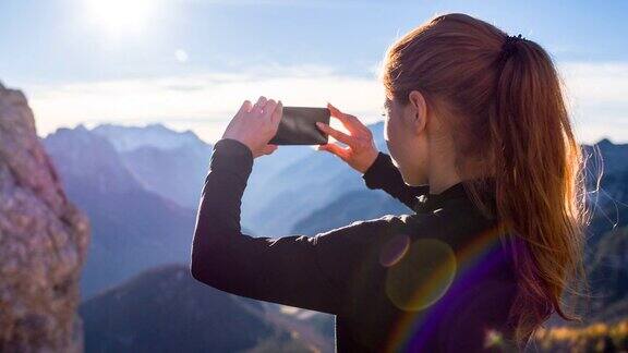年轻女子用智能手机拍山的照片
