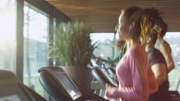 有吸引力的白人女孩在跑步机上在体育健身馆与电话和耳机