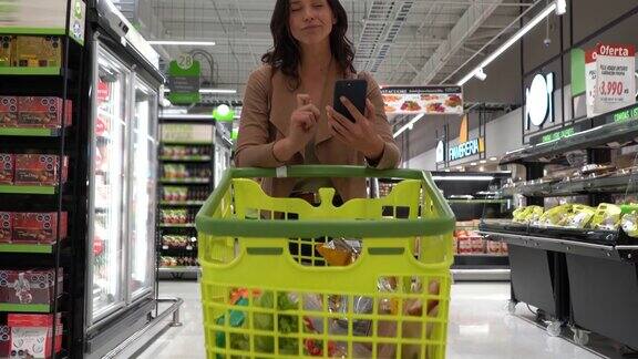 一个漂亮的女人在超市买菜看着智能手机上的购物单
