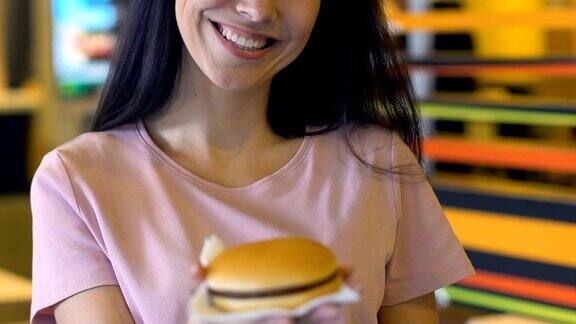 微笑的女人在镜头前展示美味和风味的汉堡肥胖的风险