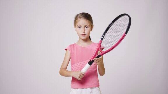 年轻的女网球运动员拿着球拍穿着粉色运动服的女孩看着相机