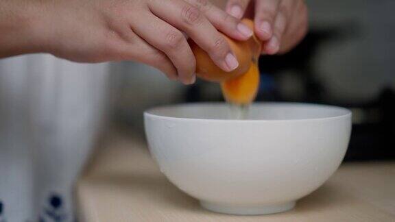 特写镜头:人类的手把鸡蛋敲到白色的碗里