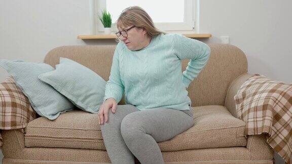 在家里的沙发上忍受背部疼痛的成熟女人