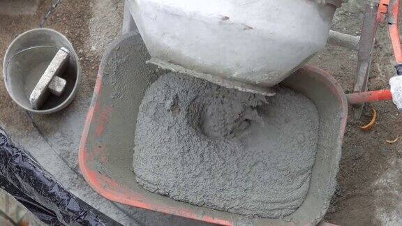 混凝土搅拌机将湿水泥倒入手推车中电动混凝土搅拌机将湿水泥倒入手推车的特写画面