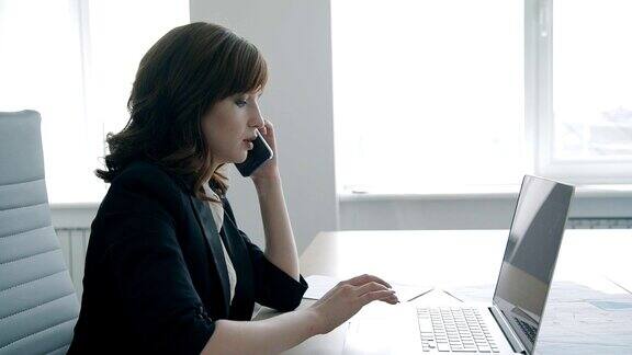 一个成功的女商人在办公室里一边打电话一边用笔记本电脑工作