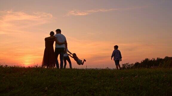 SLOMOYoung一家和三个孩子一起在日落时在草地上共度时光