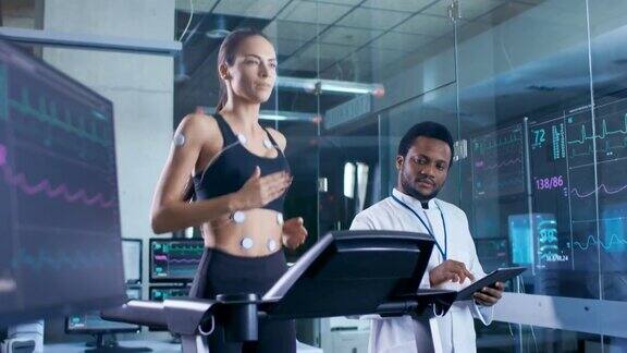 美丽的女人运动员在跑步机上跑步与电极连接到她的身体医生使用平板电脑和控制心电图数据显示在实验室监视器