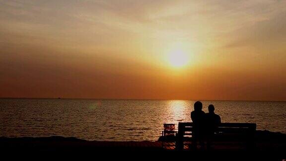 男人和女人坐在长椅上看海上的日落