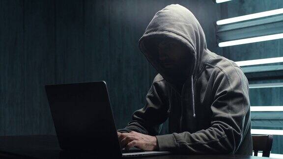 一名不知名的黑客穿着带兜帽的运动衫在笔记本电脑上输入密码
