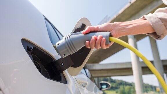 有环保意识的妇女将电动汽车的电源线插到电动汽车充电站