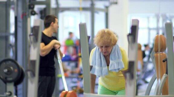 年长的女子在健身房用杠铃训练手臂
