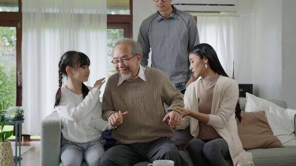 亚洲老年男爷爷坐在家中客厅的沙发沙发上进行隔离概念保健有慢性健康问题或腰痛的退休老人与家人一起