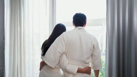 年轻夫妇穿着浴袍打开卧室的窗帘