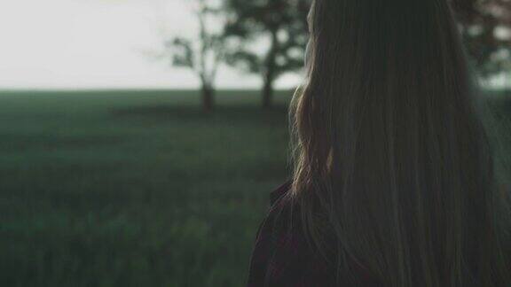 黄昏或黎明时分一个身穿红色格子衬衫的年轻女孩站在田野里头发被风吹着