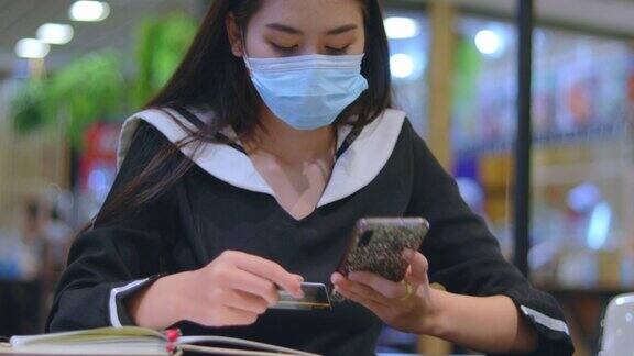 亚洲女性持有信用卡使用智能手机在家网上购物网上购物电子商务网上银行花钱她戴着面具