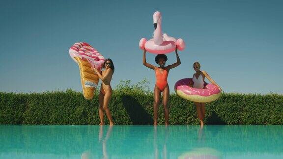 在阳光明媚的日子里穿着比基尼的多民族女性朋友们在游泳池里玩着五颜六色的充气玩具享受着暑假的乐趣