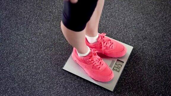 用电子秤秤体重的女孩苗条的女性腿在粉色运动鞋在数字平衡