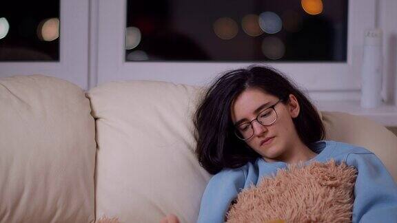 疲惫的漂亮女孩戴着眼镜深夜坐在沙发上看书镜头移动