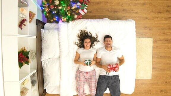 快乐的夫妇拿着圣诞礼物在床上跳从上面的观点