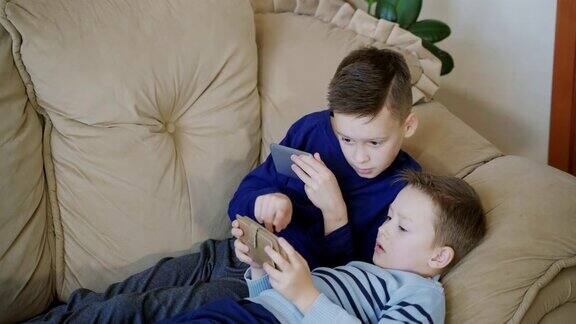 两个可爱的男孩躺在沙发上在家里玩着他的手机