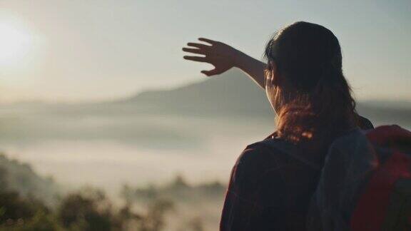一位女性徒步旅行者站在山顶上看日落