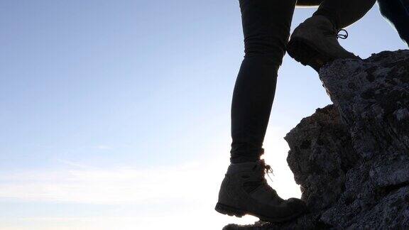 在日出时徒步者的腿爬上陡峭的岩石
