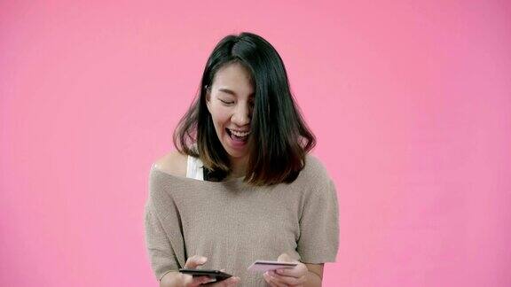 年轻的亚洲女子使用智能手机购买信用卡网上购物感觉快乐微笑在休闲服装在粉红色的背景摄影快乐的微笑可爱的快乐的女人庆祝成功