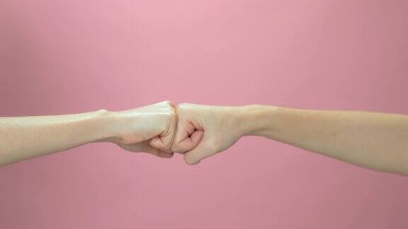 在粉红色的背景上用两只手碰拳的慢动作