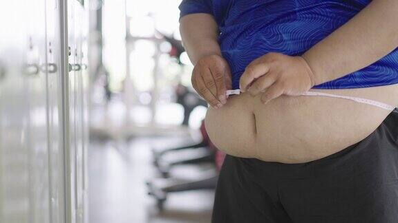 大腹便便的胖子在健身房用卷尺量腰围