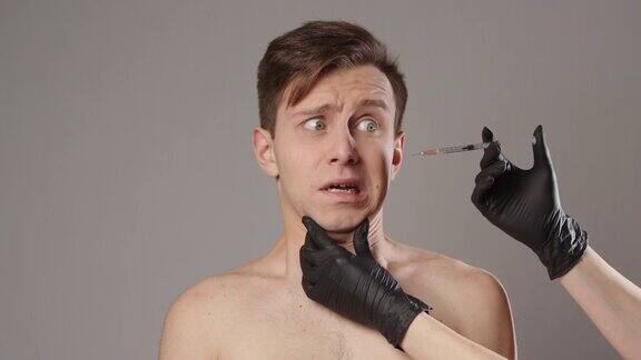 一名男子害怕戴手套的医生试图给他孤立在灰色背景上的脸注射