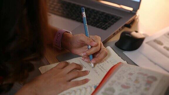 年轻的亚洲女性通过智能手机在线学习晚上在家的桌子上记笔记
